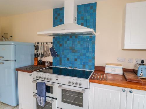 a kitchen with a stove with blue tiles on the wall at Merlin's Retreat in Tintagel