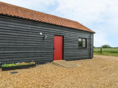 a black building with a red door and a window at Snowy Owl Barn in Shipdham