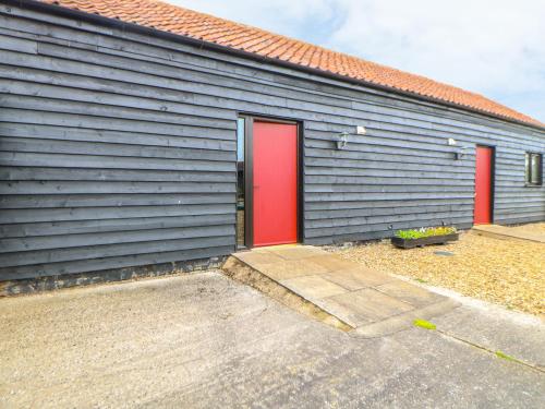 a gray building with a red door and a red at Tawny Owl Barn in Shipdham