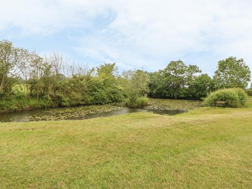 a park with a river and a bench in a field at Tawny Owl Barn in Shipdham