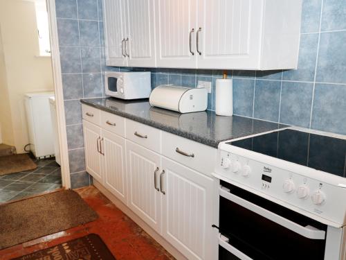 a kitchen with white cabinets and a stove top oven at Buckinghams Leary Farm Cottage in Filleigh