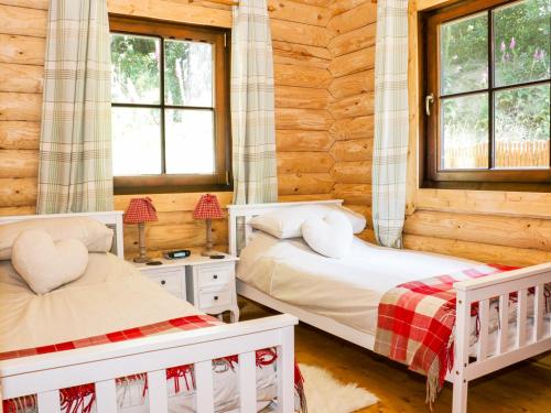 two beds in a log cabin bedroom with windows at Wilderness Lodge in Shelve