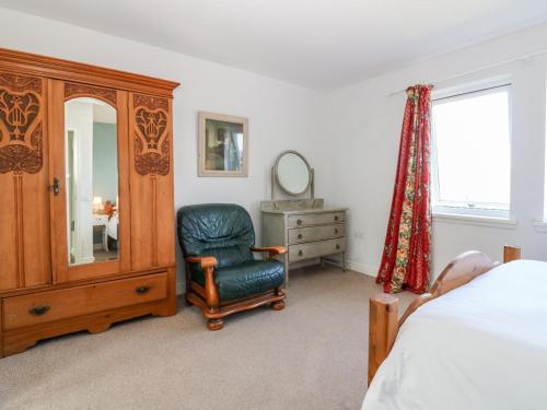 a bedroom with a bed and a chair and a mirror at Poppies Cottage in Craignure