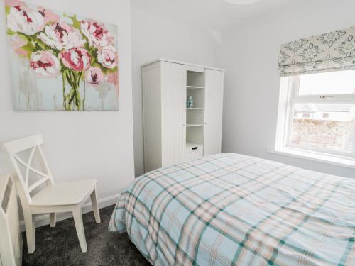 a bedroom with a bed and a chair and a cabinet at Sunnie Cottage in Seahouses