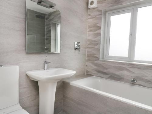 ein Badezimmer mit einem Waschbecken, einer Badewanne und einem Spiegel in der Unterkunft Upper Oaks in Windermere