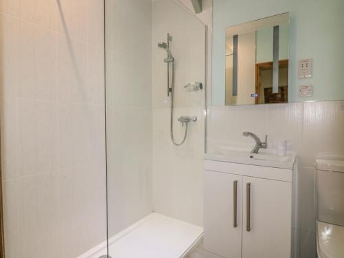 a white bathroom with a shower and a sink at Barn Cottage in Liskeard