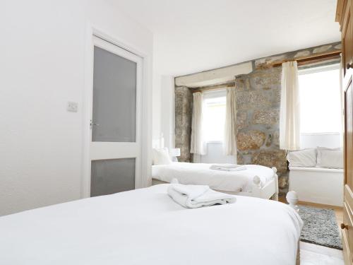 a white bedroom with two beds and a stone wall at The Coach House in Trevilley