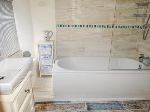 Baño blanco con bañera y lavamanos en Bobbin Cottage en Matlock