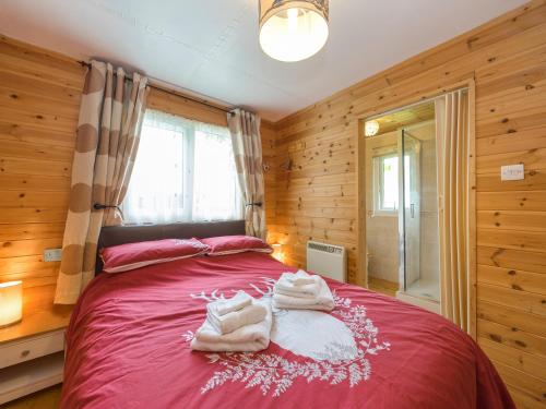 Un dormitorio con una cama roja con toallas. en The Log Cabin en Adforton