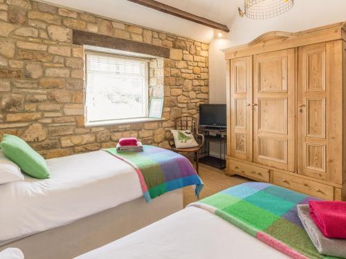 a bedroom with two beds and a stone wall at The Cowshed in Horsley