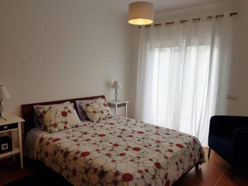 Un dormitorio con una cama con una manta de flores y una ventana en Cozy apartment in Algarve West Coast - Aljezur (2 min da Praia Monte Clérigo), en Aljezur