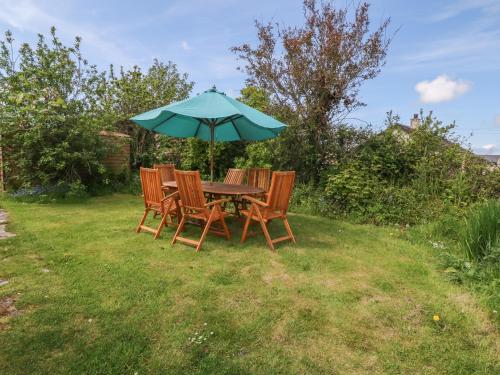 a table with three chairs and an umbrella at Minffordd in Newborough