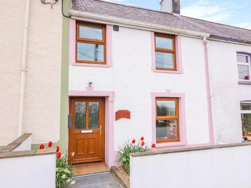 a white house with a brown door and red flowers at Bank House in Newcastle Emlyn