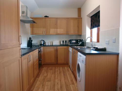 a kitchen with wooden cabinets and a washing machine at Barn View in Welcombe