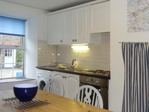 a kitchen with white cabinets and a wooden table at Kingfisher Cottage in Wadebridge