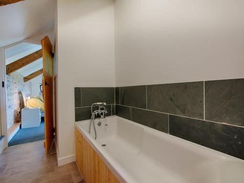 a white bath tub in a bathroom with green tiles at Salty Cottage in Morwenstow