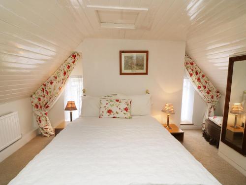 a bedroom with a white bed with two windows at Julie's Cottage in Castleisland