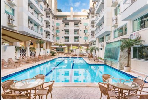 einen Pool mit Tischen und Stühlen neben einem Gebäude in der Unterkunft Bombinhas Summer Beach -Apartamento Particular in Bombinhas