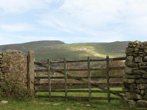 an old wooden gate with a stone wall and mountains in the background at Rushton Barn in Settle