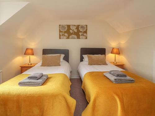 two beds in a room with yellow sheets and lamps at Knights Cottage in Maidstone