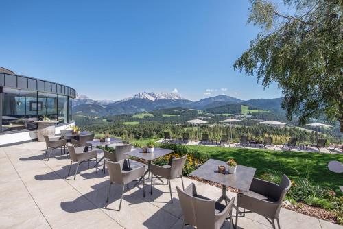 a patio with tables and chairs with mountains in the background at Panoramahotel Obkircher in Nova Ponente