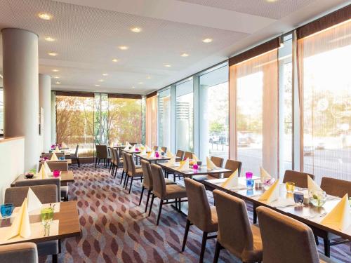 a dining room with tables and chairs and windows at Novotel Düsseldorf City West in Düsseldorf