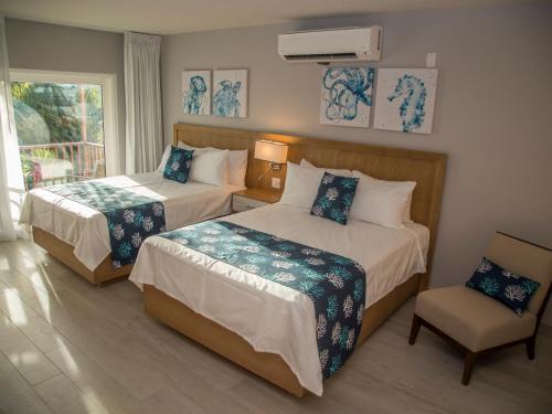 um quarto de hotel com duas camas e uma cadeira em Siboney Beach Club em Saint Johnʼs