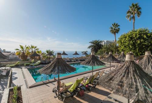 a resort with a swimming pool with straw umbrellas at The Harbour Club in Acantilado de los Gigantes