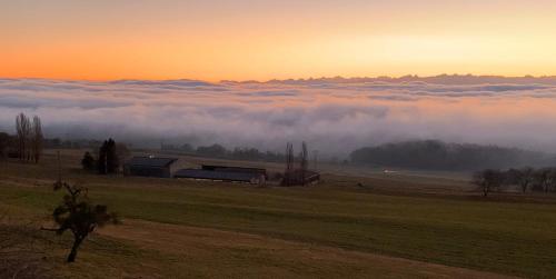 a foggy field with a barn in the distance with a view of clouds at La Ferme de la Praz - Rooms with a View in La Praz