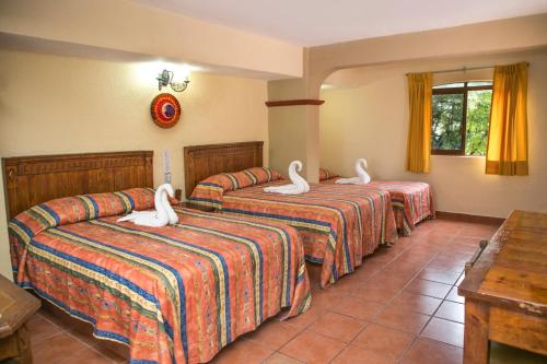 Una habitación de hotel con tres camas con cisnes. en Hotel Hacienda María Eugenia, en Acapulco