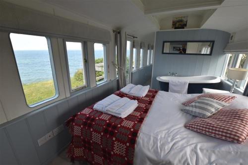 um quarto com uma cama com almofadas e o oceano em Clifftop Carriage em Aberporth