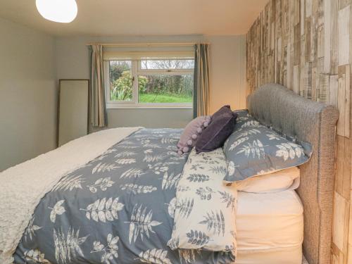 a bed with a blue and white bedspread and a window at Tidewood in Bideford