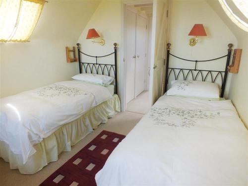 two beds in a room with white sheets at Cockshead Cottage in Saint Dogmaels
