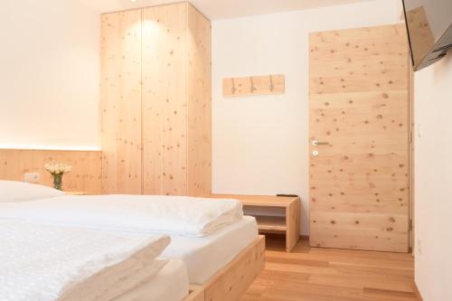 een slaapkamer met een wit bed en een houten muur bij Didi`s Appartments in Glorenza