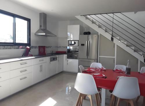 una cucina con tavolo rosso e armadietti bianchi di Villa en bord de plage a Sète