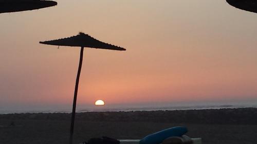 a sunset on the beach with an umbrella at Bahia Golf Beach in Bouznika