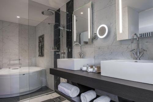 a bathroom with two sinks and a tub and a mirror at Hotel du Roi & Spa by SOWELL COLLECTION in Carcassonne