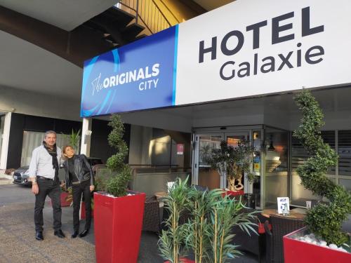 two people standing in front of a hotel lobby at The Originals City, Hôtel Galaxie, Nice Aéroport in Saint-Laurent-du-Var