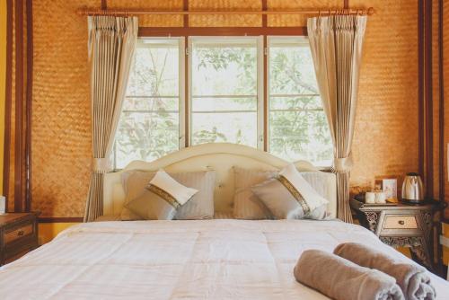 a bedroom with a white bed with a large window at Baansuan Chomchun in Amphoe Mae Taeng