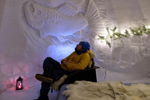 a man sitting on a bench in front of an ice wall at Lucky Ranch Snow Igloos in Pyhätunturi