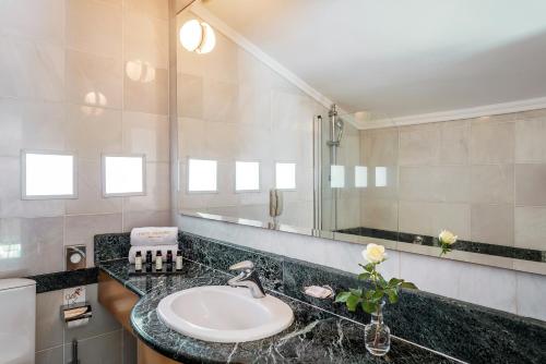 a bathroom with a sink, mirror, and tub at Mitsis Lindos Memories Resort & Spa in Líndos