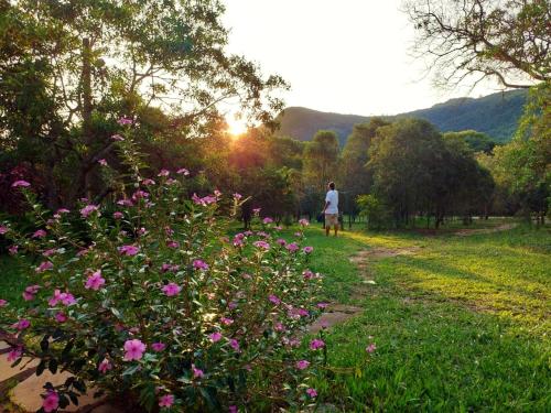 a person walking down a path with pink flowers at Camping do Delei in São Thomé das Letras