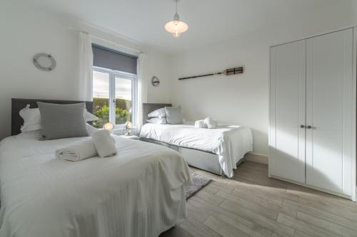 a white bedroom with two beds and a window at Miss Fishers in Port Isaac