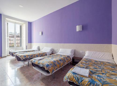three beds in a room with purple walls at Pensi&oacute;n Apolo XI in Madrid