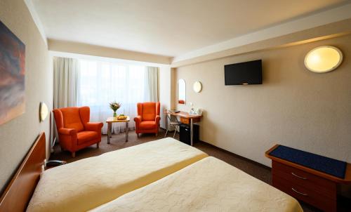 a hotel room with a bed and two orange chairs at Hotel Lux in Banská Bystrica