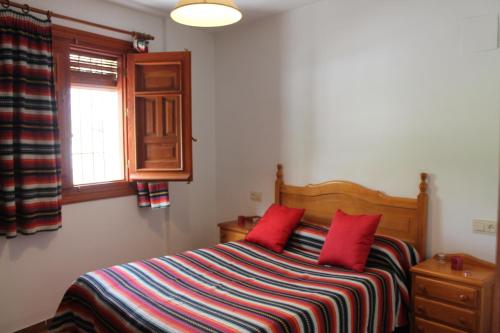 a bedroom with a bed with red pillows and a window at Apartamentos Rurales Rosendo: El Tomillo in Capileira