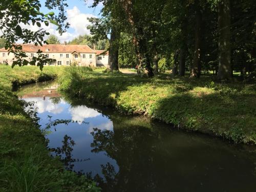 a river with a house in the background at Domaine du Plessis in Le Plessis-Luzarches