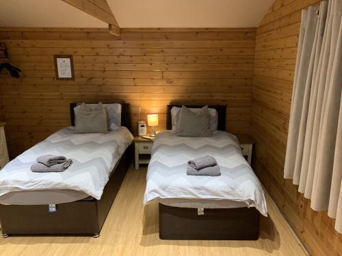 two beds in a room with wooden walls at Southernwood - Garden Lodge 2 in Didcot