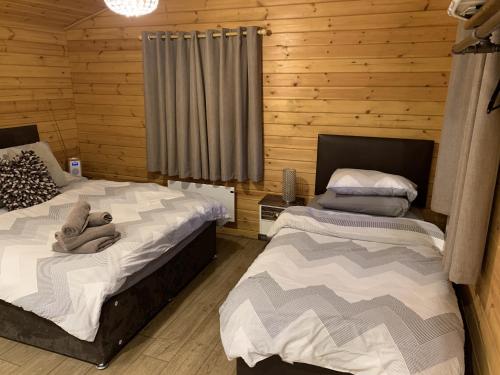 two beds in a room with wooden walls at Southernwood - Garden Lodge 9 in Didcot