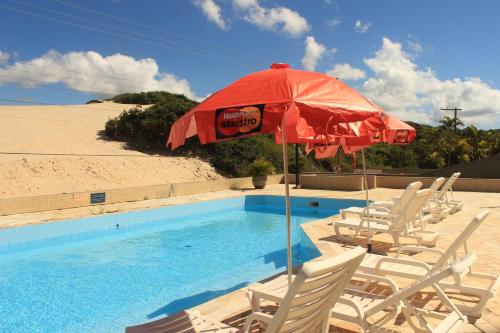 una piscina con sillas, una sombrilla y una piscina en Pousada das Dunas Via Praia Apart Hotel, en Florianópolis